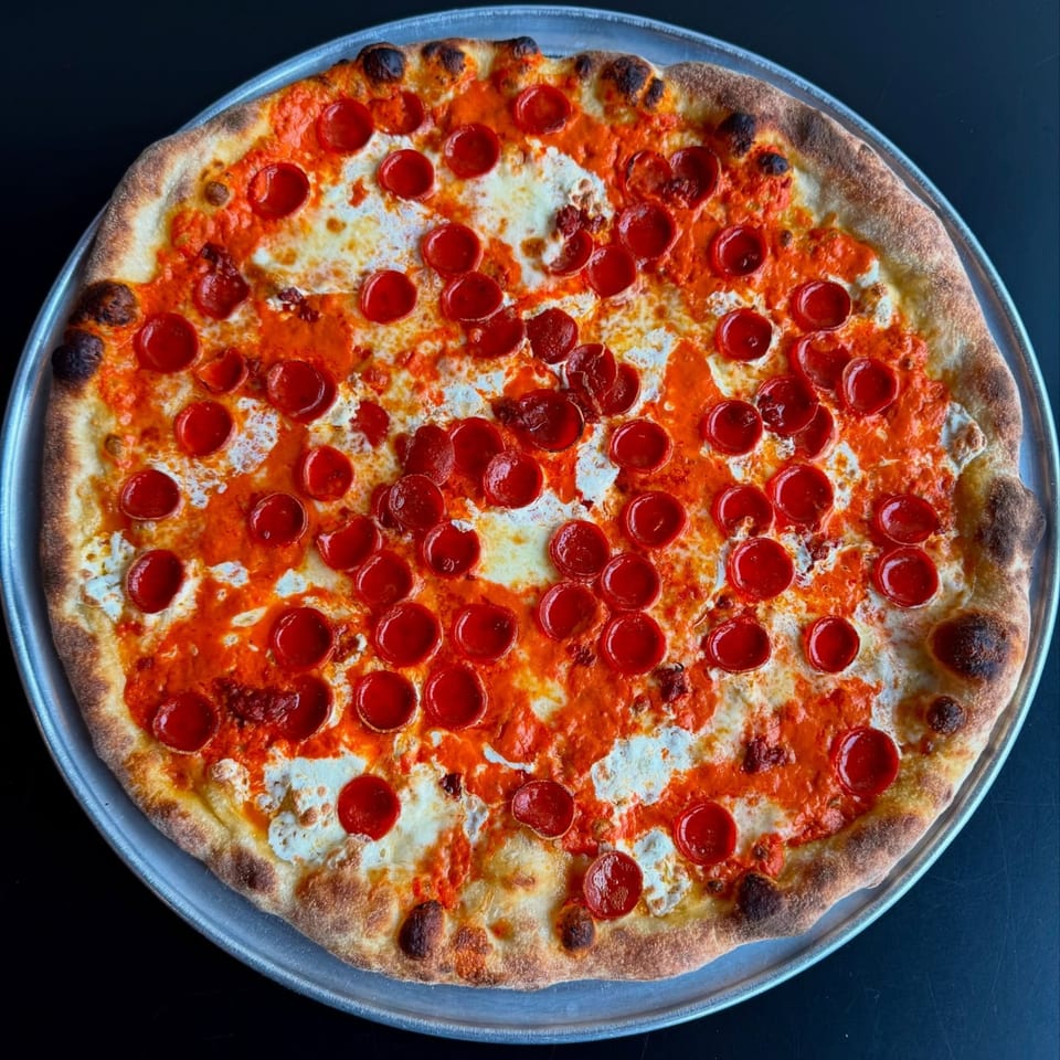 A whole pepperoni pizza with a crispy crust, red sauce, and melted white cheese on a metal tray.