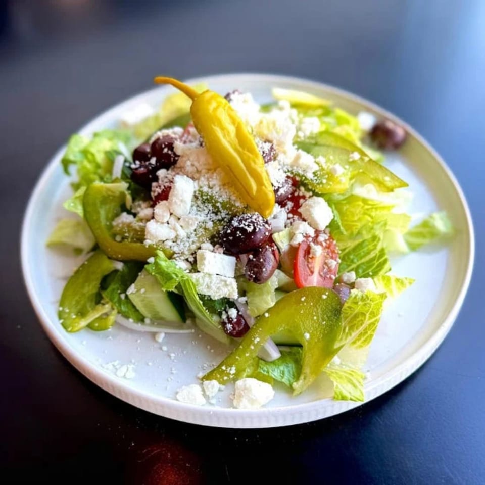A vibrant Greek salad with lettuce, tomatoes, olives, feta cheese, and a yellow pepper.