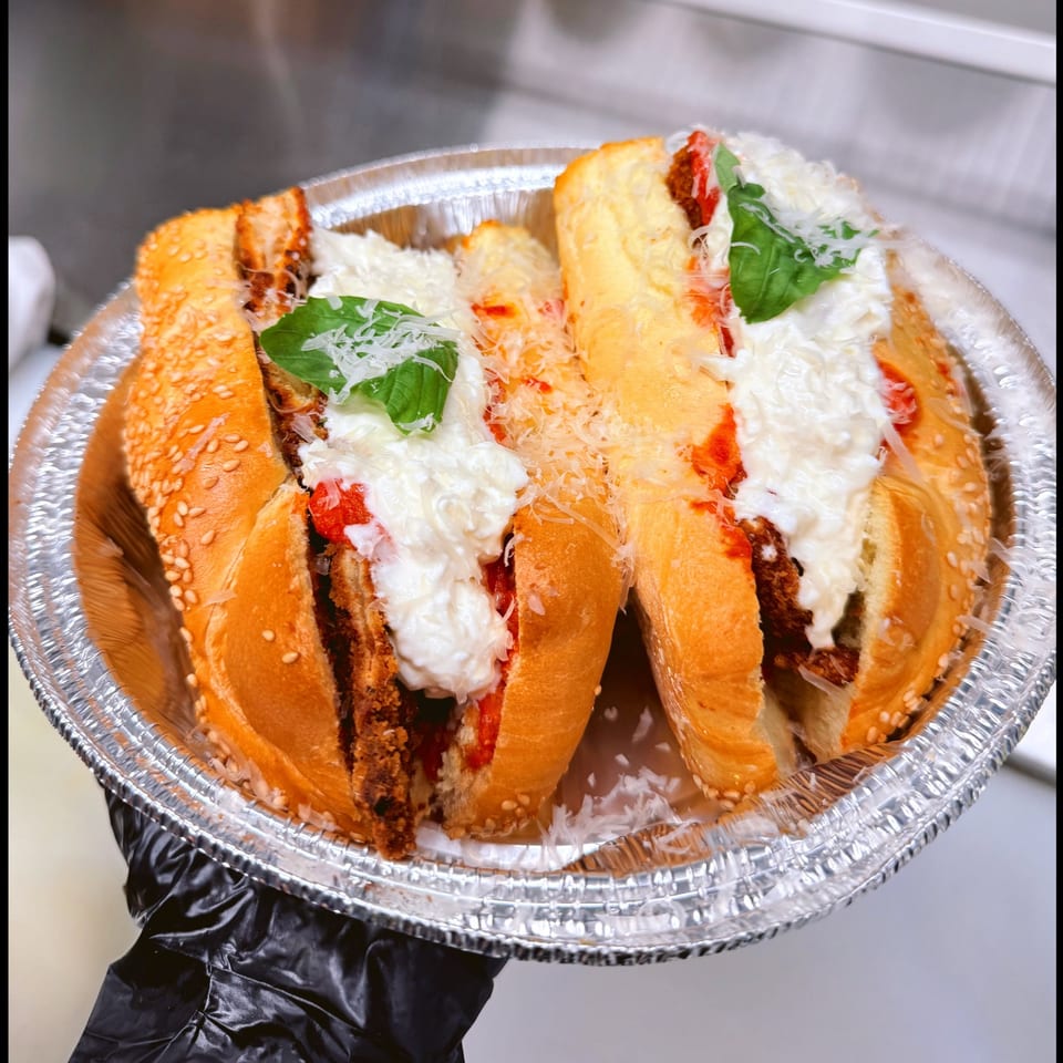 Two meatball subs with marinara, burrata, parmesan, and basil in a foil container.