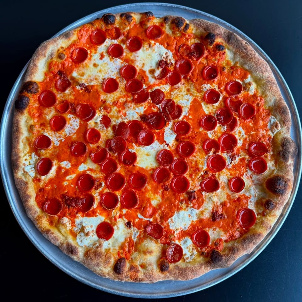 A whole pepperoni pizza with a crispy crust, melted cheese, and vibrant red sauce on a metal pan.