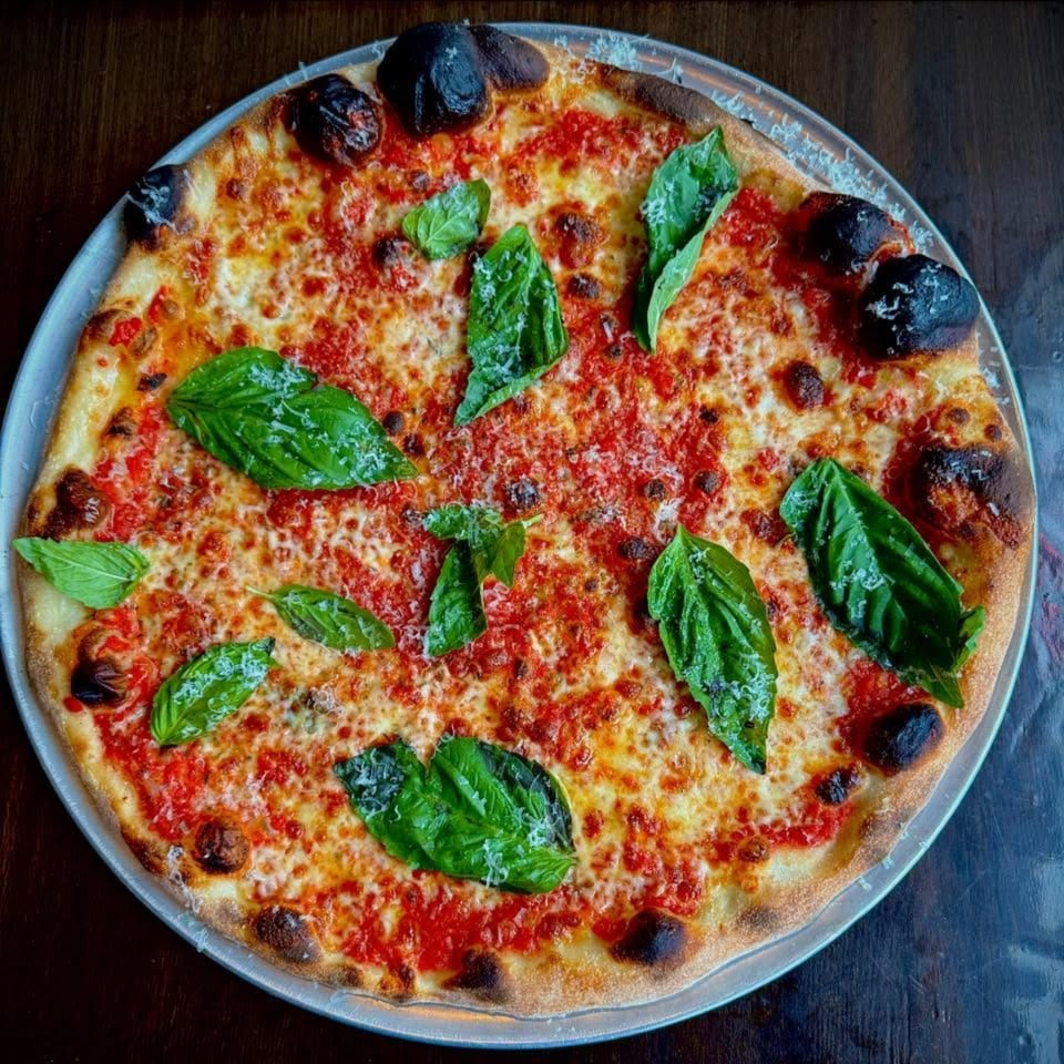 A freshly baked pizza with red sauce, melted cheese, and green basil leaves on a metal tray.