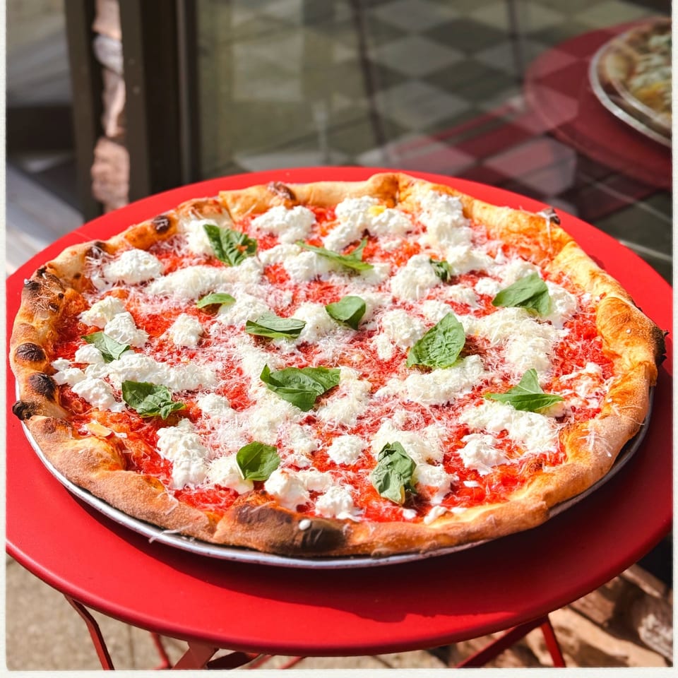 A fresh pizza with tomato sauce, ricotta cheese, grated parmesan, and basil on a red table.