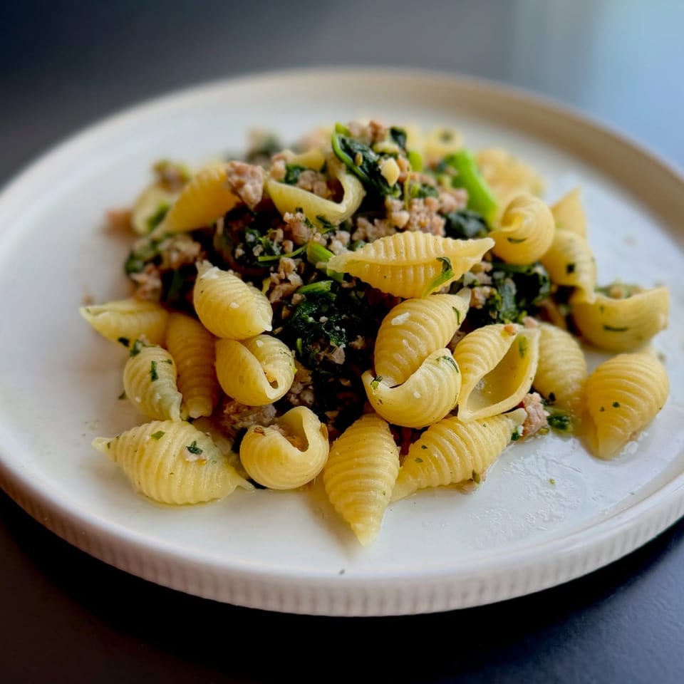 Pasta shells with ground meat and spinach on a white plate.
