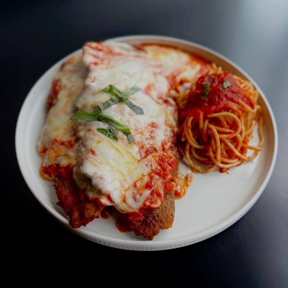 Chicken parmesan with melted cheese and tomato sauce, served with a side of spaghetti.