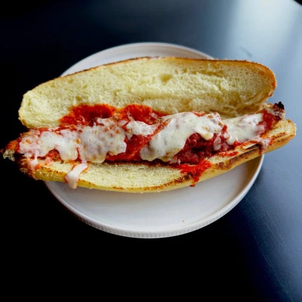 Meatball sub sandwich with melted mozzarella cheese and marinara sauce on a white plate.